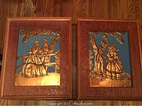 Pair of framed copper tooling art pieces showing a man and woman in period dress next to a fence and tree, with blue background and textured reddish-brown frames.
