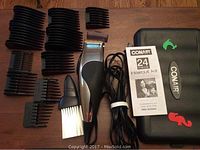 Conair haircut kit with clipper, multiple black plastic guide comb attachments, cleaning brush, oil bottle, instruction manual, and carrying case on wood floor.