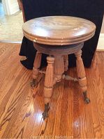 Full view of the round wooden seat and four fluted legs ending in claw feet casters.