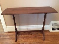 Front view of solid wood sofa table with turned legs and stretcher base on wooden floor against wall