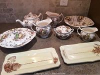 Full view of Johnson Bros Autumn Delight chinaware set with vegetable bowl, covered potato bowl, creamer, sugar bowl with lid, teapot with lid, two medium pitchers, and two rectangular platters.