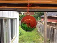 Glass ball hanging near window, showing orange and green colors with textured pattern and tied orange ribbon for hanging.