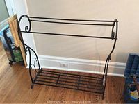 Front view of black metal blanket rack with scroll design and two upper hanging bars, plus lower slatted base for storage.
