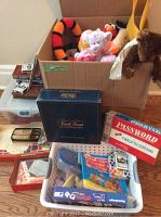 Overview of games and stuffed toys showing Password, Trivial Pursuit, game pieces, playing cards, and plush toys in boxes and containers.