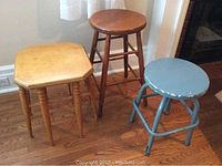 Three stools together: light wood 8-legged stool, taller darker wood stool, and grey metal stool with paint chipping.