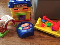 Photo of a yellow Fisher-Price plastic schoolhouse, red and white barn, blue music player, and yellow hammering toy with red hammer and colored pegs.