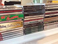 Multiple CDs stacked and lined up showing various artist compilations, Christmas songs, classical music and pop artists like Il Divo and Celine Dion