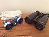 Two pairs of glasses, blue and silver opera glasses and black antique field glasses, with a white and silver pouch.