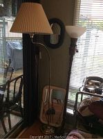 Metal floor lamp with beige pleated fabric shade and wood turned lamp with white textured glass shade next to window, two wall mirrors visible on wall