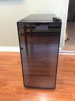 Front view of wine chiller with closed glass door showing three icons near top center and a black frame.