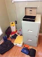 Overview of office lot showing the filing cabinet, calculators, keyboard, cash box on top, paper supplies, laptop bag, and cables on a wooden floor