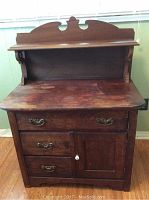Front view of antique wooden wash stand showing drawers, cabinet door and decorative backboard.