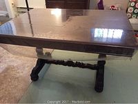 Full view of the antique dining table with solid wood rectangular top protected by plastic cover and thick decorative base.