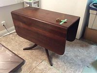 Wood rectangular drop leaf table closed, polished dark wood surface, shows brass bracket on top and key taped on the surface.