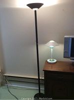 Photo showing the 71 inch black metal floor lamp standing next to a wooden desk with the smaller white table lamp on top.