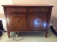 Front view of solid wood cabinet showing two drawers and two doors with brass handles and tapered legs