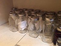 Photo of approximately 30 clear glass Bernardin 1L mason jars with metal lids, arranged on shelf.