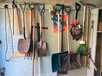 Hanging yard tools including shovels, snow shovels, coiled extension cord, broom, and come-along on wall hooks.