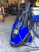 Front angle photo of the Simonize electric pressure washer with vacuum functionality, showing blue and black plastic body and handle with hose attached.