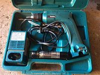 Cordless power drill in turquoise with no battery attached, placed inside turquoise carrying case along with a black rechargeable battery and charger with power cord.