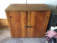 Front view of the pine storage cupboard with closed double doors showing wood grain and metal latches.