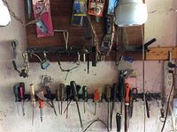 Wide view of various hand tools hung on wall-mounted rack, including screwdrivers and pliers.