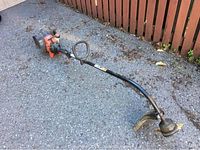 Full view of the Yard Machines gas-powered weed wacker showing the straight shaft, loop handle, cutting head with protective guard, and orange/black engine housing.