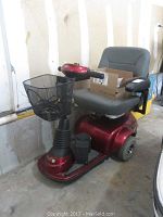Right-front perspective of red Invacare scooter showing seat, basket and chassis.
