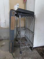 Chrome metal shelving unit with 3 wire shelves and a black car emergency repair kit on top, next to a boxed shelving unit.