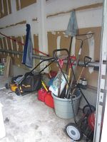 Photo showing lawn mowers, garden tools in a garage corner with gas cans