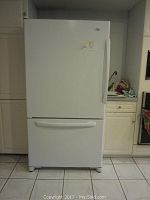 Front view of white Amana refrigerator with bottom freezer drawer in a kitchen setting.