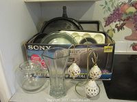 Photo of several glassware items, decorative light covers, and a box with Sony label containing various kitchen items.