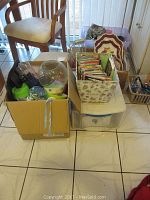 Multiple boxes and bins filled with assorted kitchen items including glass jars, plastic containers, cookbooks, and serving platters