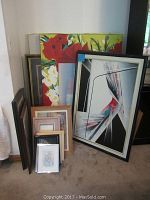 Multiple framed wall art pieces including large floral and abstract paintings arranged against a wall.