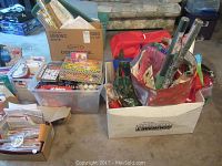 Full view of the lot showing various boxes, bins, gift bags, and rolls of wrapping paper in two large containers placed on floor.