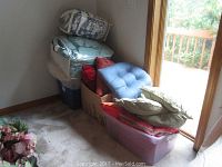Stack of assorted pillows in different colors and comforters in bags and bins near sliding glass door