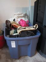 Blue plastic bin filled with assorted handbags, showing various sizes, materials, and colors including a bright pink handbag and a straw woven tote