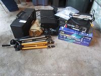 Photo showing various electronics and equipment including a black stereo cassette deck, black JVC box, tripods, and cables.