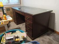 Full view of dark wooden office desk with six drawers (three on each side) and glass top, sitting on a carpeted floor near a window.