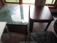 Photo showing marble top end table with dark wood base next to a dark wood end table with rounded edges, both near a window.