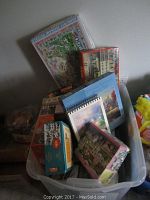 Bin containing several jigsaw puzzles with visible box art showing buildings and landscape images.