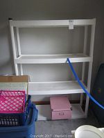 4-tier white plastic shelving unit against a wall with a pink box and some storage baskets nearby.
