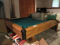 Wide view of the pool table showing wooden frame and green felt top, items on top of table, located in basement