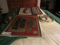 Five plus pieces of vintage beer-themed wall art and decor laid out on a pool table including framed signs and a beer light clock.
