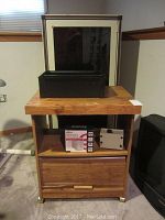 View of vintage Fisher speakers stacked on wheeled TV stand with wooden finish, computer cabinet behind it.