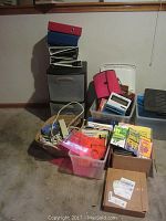 Photo of assorted office supplies including binders atop a black two-drawer fire safe with plastic drawers, plastic storage bins filled with documents, books and office items, and a red zippered organizer case.