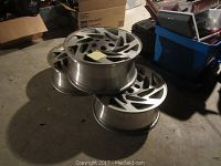 Three stacked 17-inch alloy car rims with the side view showing the depth and spokes of the rims. Surrounding area is a garage floor with boxes and containers.