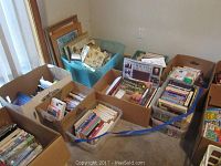 Wide shot showing multiple boxes and bins filled with assorted books, magazines, DVDs, and picture frames stacked and organized