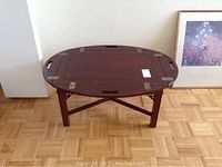 Front view of oval wood coffee table showing the adjustable top with metal brackets on corners and the wood grain surface.