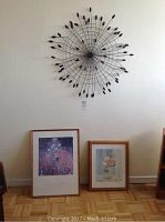 Room view showing black metal wall hanging mounted on wall above two framed posters resting on floor